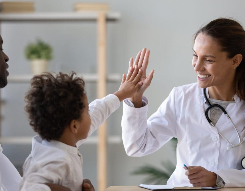 Smiling young female pediatrician give high five to little african American boy at consultation in clinic, happy woman doctor consult biracial toddler kid in hospital. Children healthcare concept